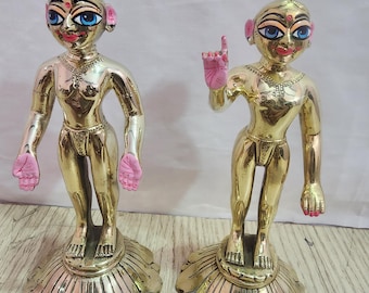 May include: Two gold-colored statues of deities standing on lotus-shaped bases. The statues have painted blue eyes, pink ears, and pink hands.