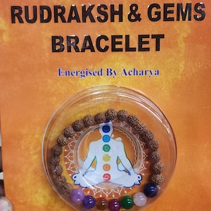 May include: A brown rudraksha and gems bracelet with seven colorful gemstones. The bracelet is displayed in a clear plastic container with a background image of a person meditating with seven chakras.