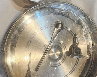 May include: A silver metal puja thali set with a small bowl, a spoon, a bell, and a small pitcher. The set is packaged in plastic wrap.