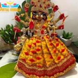 Puede incluir: Una estatua dorada de una deidad hindú con múltiples brazos, vestida con un vestido estampado en amarillo y rojo y una corona. La estatua está sentada sobre un toro dorado.