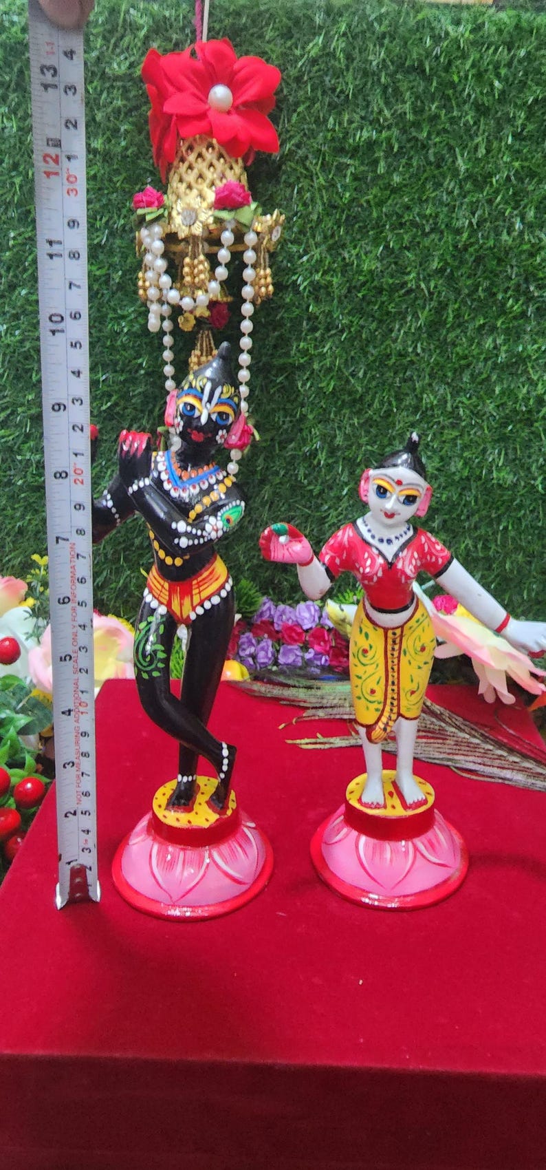 Op de afbeelding: Twee handgeschilderde beeldjes van hindoe&iuml;stische goden, Krishna en Radha, staand op lotusvormige bases. Krishna speelt fluit en Radha houdt een bloem vast. De beeldjes zijn geschilderd in levendige kleuren, waaronder zwart, rood, geel en groen.
