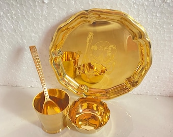 May include: A gold-colored metal serving set with a round tray, two bowls, a cup, and a spoon. The tray has a decorative design in the center.