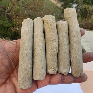May include: Five cylindrical clay objects, possibly pottery, are held in a hand. The objects are a light brown color and have a rough texture.