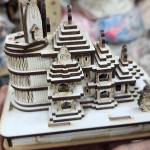 May include: A detailed wooden model of a multi-level building with intricate details and a white base.