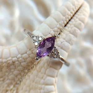 Peut inclure: Une bague en argent avec une améthyste de forme marquise et de plus petites pierres claires sur la bande.