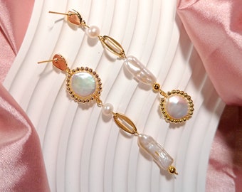 May include: A pair of gold earrings with pearl accents. Each earring features a large, round pearl surrounded by a gold beaded border. The earrings are suspended from a gold chain with smaller pearls and gold links.