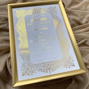 May include: A white wedding invitation with gold calligraphy and floral designs. The invitation includes the names "Murat Akbar" and "Afra Darak" and the date "13 April 2024".
