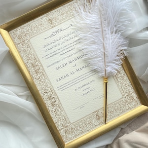 Peut inclure: Un certificat de mariage encadré avec une bordure dorée et un motif ornemental. Le document présente des caractères arabes et une traduction anglaise, avec les noms SALEH MAHMOOD et SANAH AL-MANSOOR. Une plume blanche avec une base dorée repose sur le cadre.