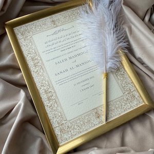 Könnte beinhalten: Eine gerahmte Heiratsurkunde mit goldenem Rand, mit kunstvoller Kalligraphie und den Namen SALEH MAHMOOD und SANAH AL-MANSOURI. Ein weißer Federhalter mit goldenem Fuß ruht auf der Urkunde. Das Datum ist der 21. Dezember 2025.