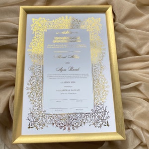 May include: A gold-framed wedding certificate with ornate calligraphy and floral designs. The text reads "Morat Abbas and Azra Barak" and includes the date "13 April 2024" and the location "In the City of Manchester".