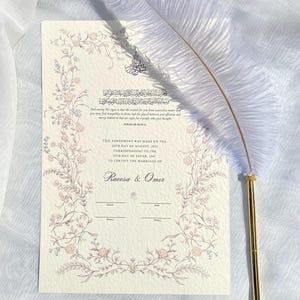 May include: A wedding certificate with floral border and text, "THIS AGREEMENT WAS MADE ON THE 20TH DAY OF AUGUST, 2021...TO CERTIFY THE MARRIAGE OF Racesa & Omer." A white feather pen with a gold-coloured tip rests on the certificate.
