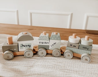 May include: A wooden toy train with five cars. The cars are painted in shades of gray and green and feature different designs. The first car says "Jannes", the second car says "13-08-2023", the third car says "3:55 Uhr", the fourth car says "51 cm", and the fifth car says "3320 g".