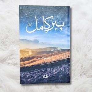 Puede incluir: Una portada de libro con un fondo de cielo azul estrellado. El título del libro es "بيكاهل" en escritura árabe. La portada también presenta un paisaje con colinas y un campo de hierba.