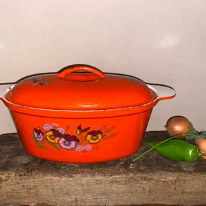 Puede incluir: Plato de horno ovalado naranja con tapa blanca y diseño floral. El plato tiene asas blancas a los lados y un diseño floral de pensamientos morados, amarillos y marrones.