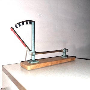 May include: A vintage wooden base with a metal lever and a graduated scale. The lever is attached to a metal rod that is supported by two metal brackets. The scale is marked in degrees.