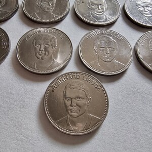 Peut inclure: Une collection de huit pièces commémoratives argentées représentant des portraits de joueurs de football allemands. Chaque pièce porte le nom d'un joueur différent et une bordure surélevée.