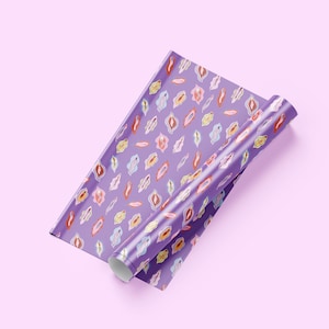 May include: A roll of wrapping paper featuring a repeating pattern of stylized vulva illustrations in various colors including red, pink, yellow, and blue, set against a solid purple background. The paper is partially unrolled to show the design.