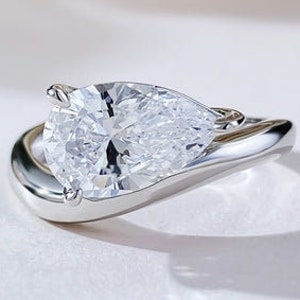 May include: A pear-shaped diamond engagement ring set in a white gold band. The ring features a unique, twisted design.