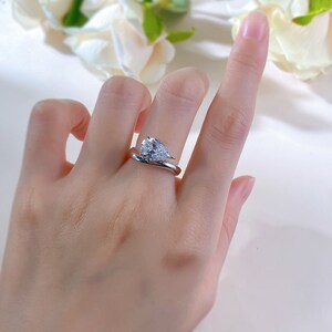 May include: A silver ring with a pear-shaped clear gemstone set in a twisted band.
