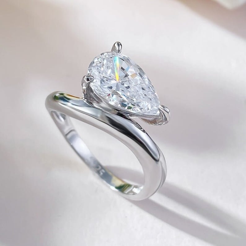 May include: A silver ring with a pear-shaped diamond set in a twisted band.