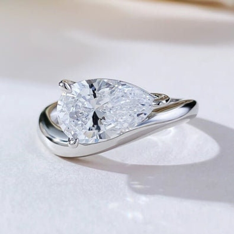May include: A pear-shaped diamond engagement ring set in a white gold band. The ring features a unique, twisted design.