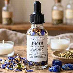 May include: A clear glass dropper bottle labeled Magick & Sage Thoth Ritual Oil, God of Wisdom, Writing, & Knowledge, containing oil with blue petals. The bottle sits on a wooden surface with loose blue petals, two blue stones, and white candles.