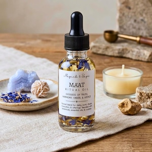 May include: A clear glass dropper bottle filled with golden oil and blue flower petals. The white label reads Magick & Sage MA'AT RITUAL OIL GODDESS OF TRUTH, HARMONY, ORDER, & JUSTICE. Sacred blend for deity work, rituals, invocation, & offerings.