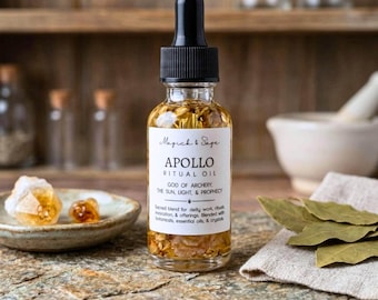 May include: A clear glass dropper bottle filled with golden ritual oil containing visible botanicals. The white label reads Magick & Sage, APOLLO RITUAL OIL, GOD OF ARCHERY, THE SUN, LIGHT, & PROPHECY, and Sacred blend for deity work, rituals.