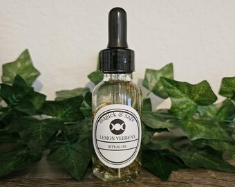May include: A clear glass dropper bottle with a black cap containing liquid. The white oval label features the text "magick & sage", a triple moon symbol, "LEMON VERBENA", and "RITUAL OIL" in black ink. The bottle is filled with a light-colored oil.