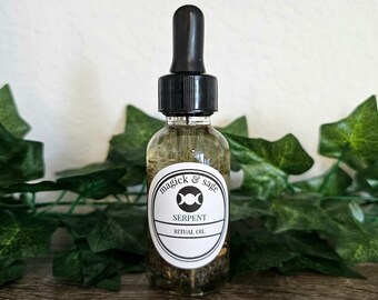 May include: A clear glass dropper bottle filled with oil and botanical pieces. The white oval label features the text "magick & sage", a triple moon symbol, and the words "SERPENT RITUAL OIL" in black ink. The bottle has a black dropper cap.