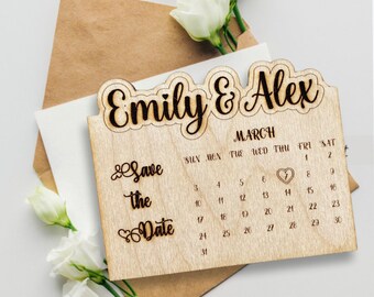 Puede incluir: Calendario de madera para guardar la fecha con los nombres "Emily & Alex" y la fecha "7 de marzo" resaltada. El calendario está hecho de madera marrón claro y tiene un aspecto rústico.