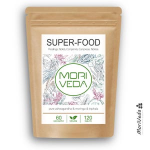 Op de afbeelding: Een bruine papieren zak met MoriVeda Super-Food tabletten. Het etiket bevat de tekst "SUPER-FOOD" en "MORI VEDA" in een groene cirkel. Het vermeldt ook "pure ashwagandha & moringa & triphala", met 120 tabletten en een voorraad voor 60 dagen.