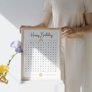 May include: A framed "Happy Birthday" word search puzzle. The top of the frame has the words "Happy Birthday" in a handwritten font, with a rainbow illustration. The puzzle is a grid of letters with a gift box illustration at the bottom.