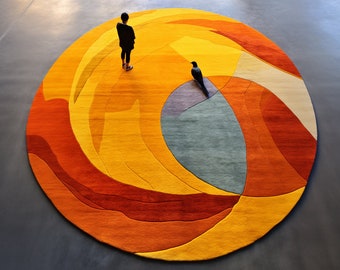 May include: A round, abstract rug with a swirling pattern in shades of orange, yellow, red, and blue. The rug is on a gray floor and a person is standing near it.