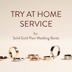 May include: Try at Home Service for Solid Gold Plain Wedding Bands. A selection of gold wedding bands in various styles and colours are shown on a light beige surface.