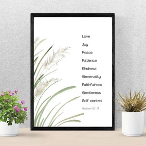 K&ouml;nnte beinhalten: Ein gerahmter Druck mit einer Aquarell-Illustration von gr&uuml;nem Gras und wei&szlig;en Blumen. Der Druck zeigt eine Liste von Tugenden: Liebe, Freude, Frieden, Geduld, Freundlichkeit, Gro&szlig;z&uuml;gigkeit, Treue, Sanftmut und Selbstbeherrschung. Der Text "Galater 5,22-23" ist unten gedruckt.