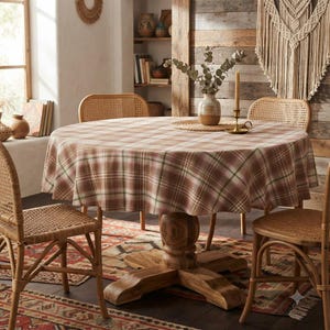 May include: A round wooden dining table covered with a plaid tablecloth in shades of brown, cream, and green. The table is surrounded by four light brown rattan chairs with woven seats. A ceramic vase with eucalyptus branches sits on the table.