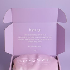 May include: A light purple cardboard shipping box containing a soft pink satin pouch. The box lid features the text UNCOMMON WIGS and a thank you note. The pink pouch is printed with the text UNCOMMON WIGS LUXURY HUMAN HAIR WIGS in white.