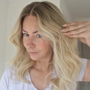 May include: Shoulder-length hair with a center part, featuring a gradient color transition from dark brown roots to a bright platinum blonde shade. The hair has a wavy texture with loose curls and is styled in a natural, voluminous appearance.