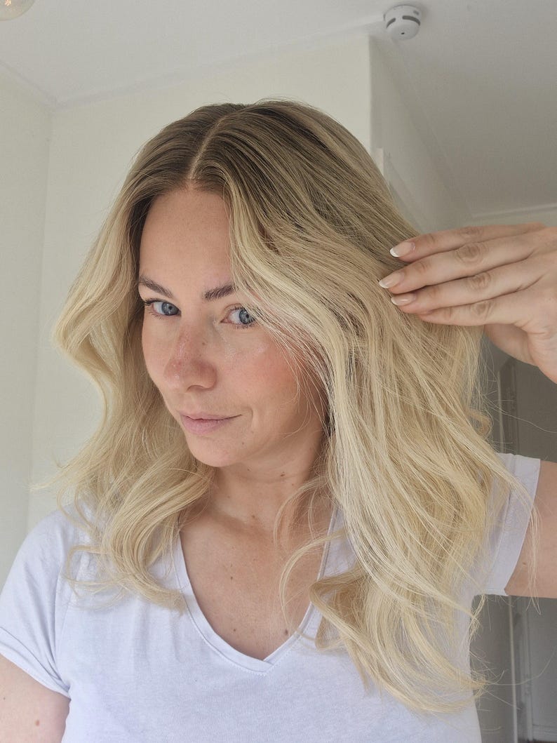May include: Shoulder-length hair with a center part, featuring a gradient color transition from dark brown roots to a bright platinum blonde shade. The hair has a wavy texture with loose curls and is styled in a natural, voluminous appearance.