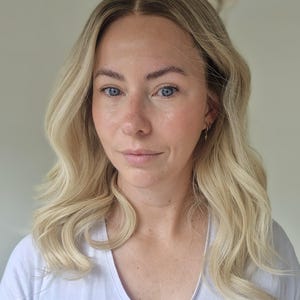 May include: A shoulder-length blonde wig with a center part and soft, loose waves. The hair features a natural-looking root transition from a darker shade to a bright, light blonde tone, styled with a smooth texture and a subtle, layered finish.