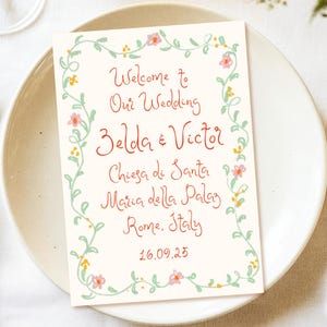 May include: A wedding invitation with a floral border. The text reads "Welcome to Our Wedding Zelda & Victor Chiesa di Santa Maria della Palaz Rome, Italy 16.09.25".