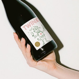May include: A bottle of red wine with a label that says "TWINKLE" and features a cartoon elf holding a glass of wine. The label also says "Craft Twinkle Wine".