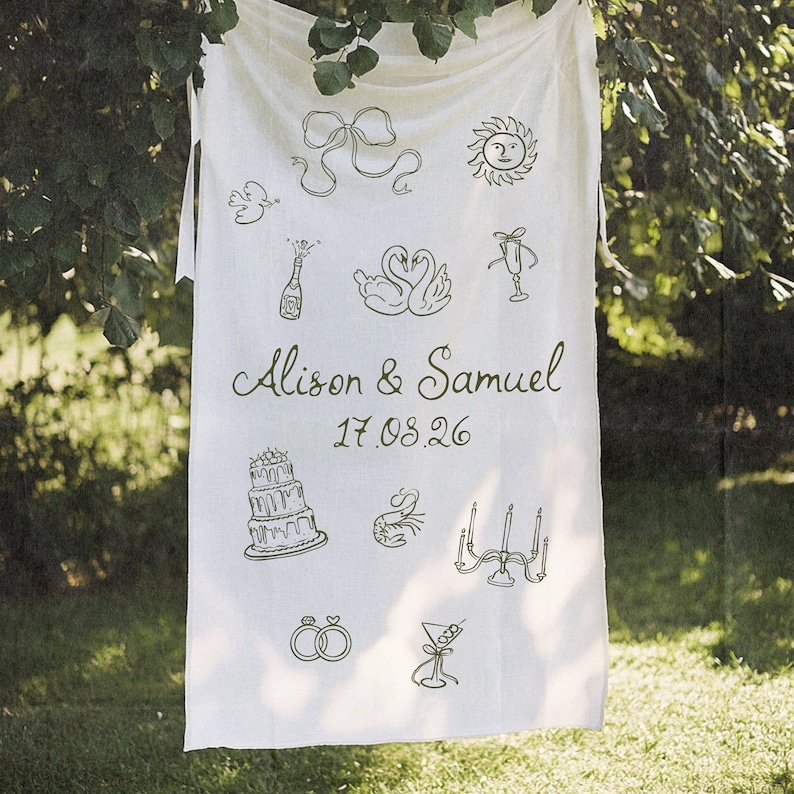 May include: White fabric banner with black line drawings of wedding-themed icons, including a cake, swans, champagne, rings, and candles. The banner also includes the text "Alison & Samuel 17.08.26".
