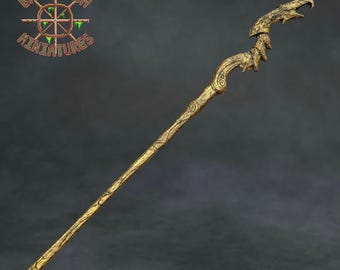 May include: A gold-colored staff featuring a textured, bark-like shaft and a top section shaped like a stylized bird head with sharp, curved features. The logo Baelstrom Miniatures is visible in the upper left corner of the image.