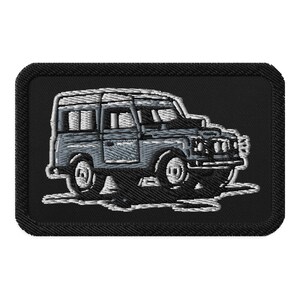 Op de afbeelding: Geborduurde patch met een lichtblauwe terreinwagen met witte omtrek op een zwarte achtergrond. De patch is rechthoekig met afgeronde hoeken. Het voertuigontwerp omvat ramen, wielen en een dakdrager.