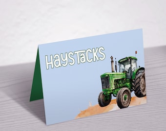 May include: A blue and green place card with the text "Haystacks" in green letters. A green and black tractor is pictured on the right side of the card.