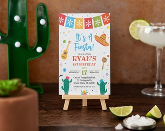 Op de afbeelding: Een kleurrijke uitnodiging voor een 1e verjaardagsfeest met de tekst "Het is een Fiesta! Ryan's 1e verjaardag" en details over het feest, inclusief de datum, tijd en locatie. De uitnodiging bevat een sombrero, maracas, een gitaar en cactussen.