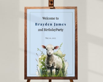 May include: Welcome to Brayden James's 2nd Birthday Party sign with a cute white lamb illustration on a light blue background. The sign is framed in wood and is ready to be displayed at a party.