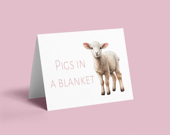 Puede incluir: Una tarjeta blanca con el texto "PIGS IN A BLANKET" impreso en rojo. Un cordero blanco aparece en el centro de la tarjeta.